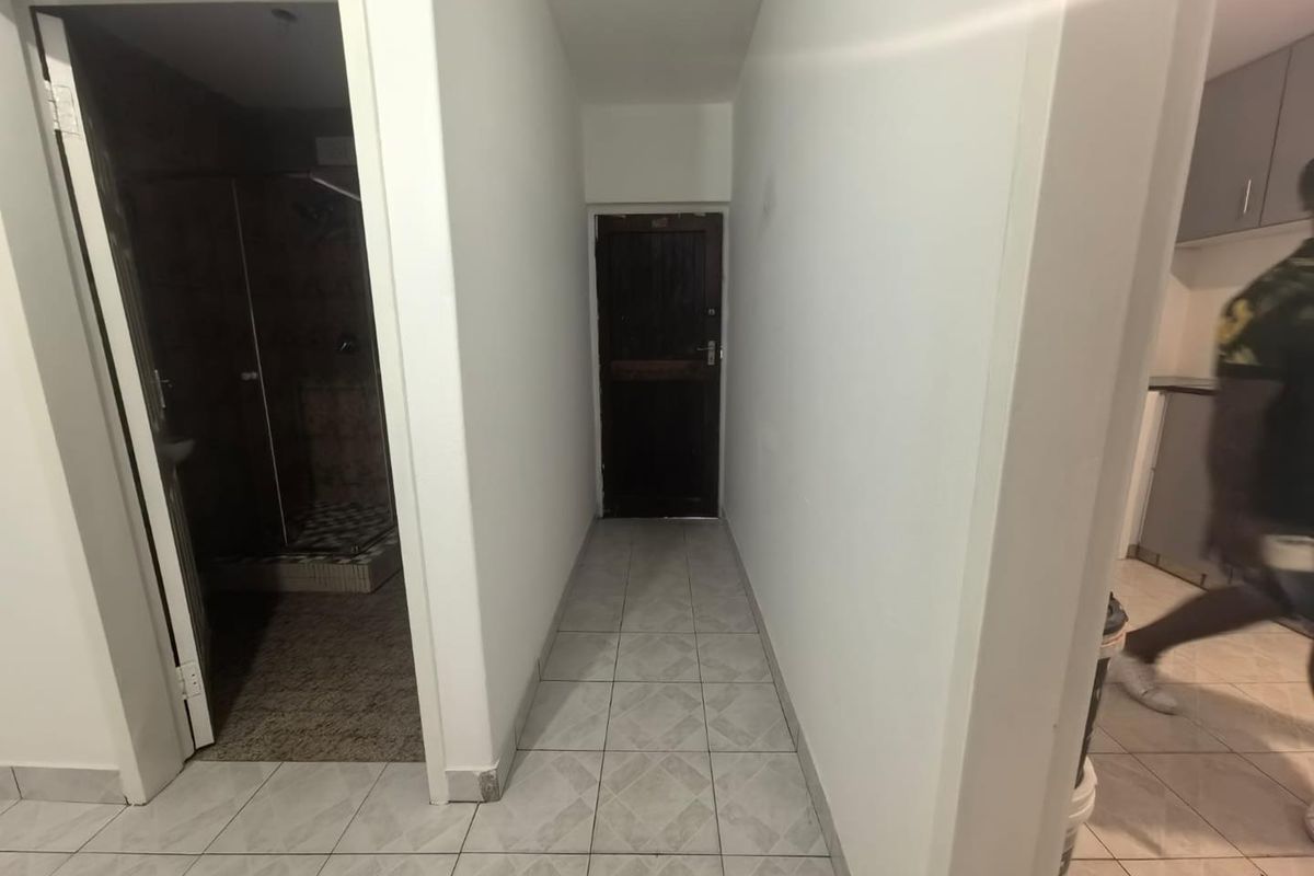 A functional hallway with tiled flooring providing access to adjacent rooms, including a bathroom and kitchen area.