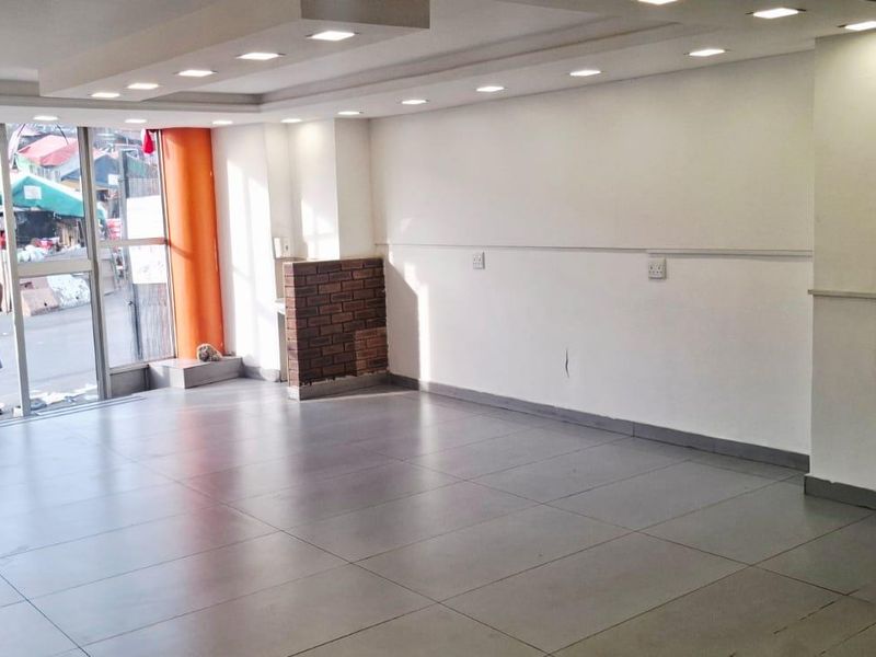 A spacious, empty open-plan commercial unit featuring large glass frontage, recessed ceiling lighting, and durable tiled flooring, suitable for various retail or office uses.