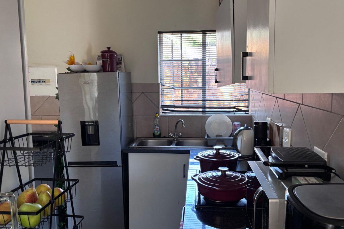 Compact kitchen featuring built-in cabinetry, a double sink with mixer tap, tiled backsplash, and an electric hob.