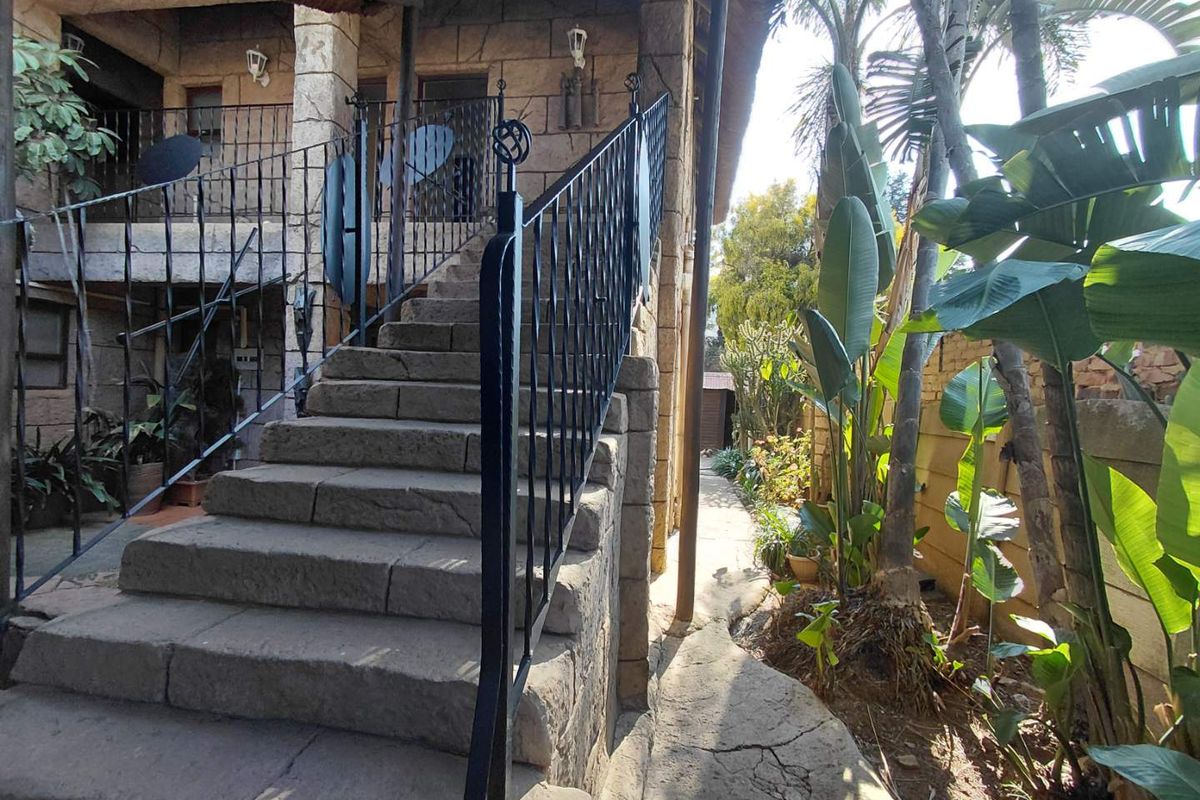 Exterior view of a stone-clad staircase with wrought iron railings leading to an upper level, set within a landscaped garden area.