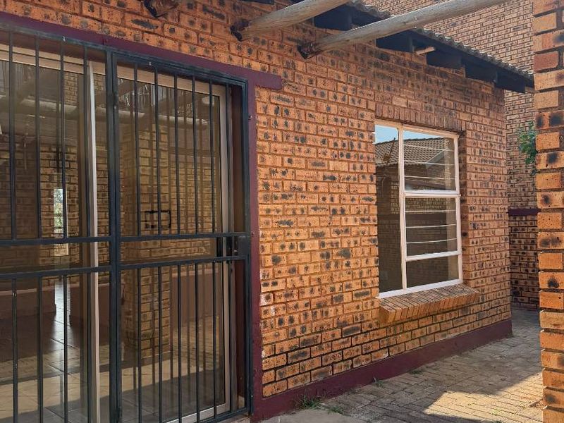 A covered patio area featuring a timber pergola, facebrick walls, and tiled flooring, providing a functional outdoor space with secure access to the interior.