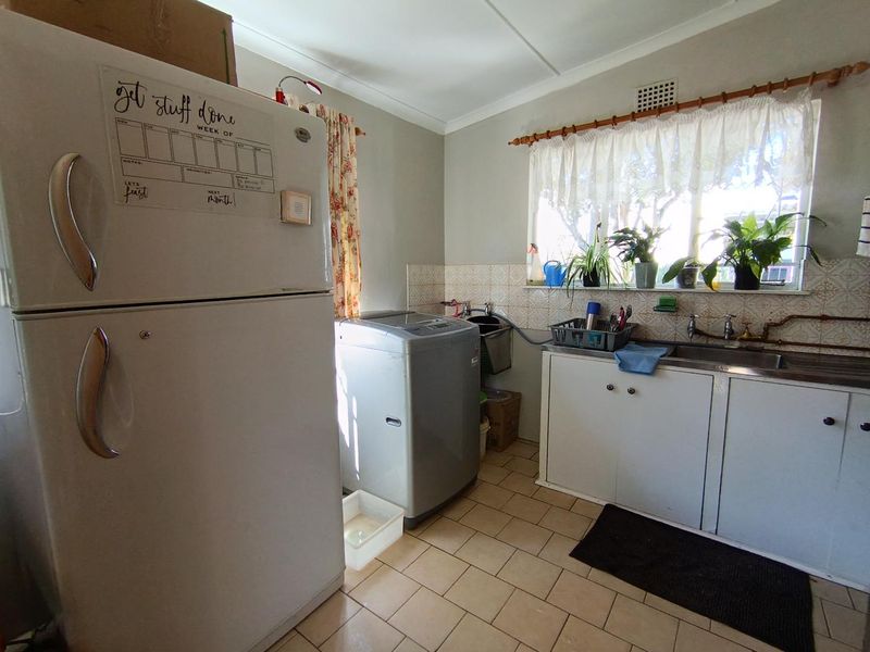 A functional laundry room featuring a stainless steel sink, tiled splashback, and built-in cabinetry with ceramic floor tiles.