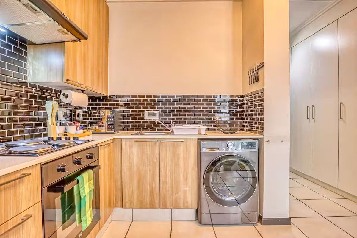 A functional kitchen featuring light wood cabinetry, dark subway tile backsplash, built-in oven, gas hob, and integrated laundry space with tiled flooring.