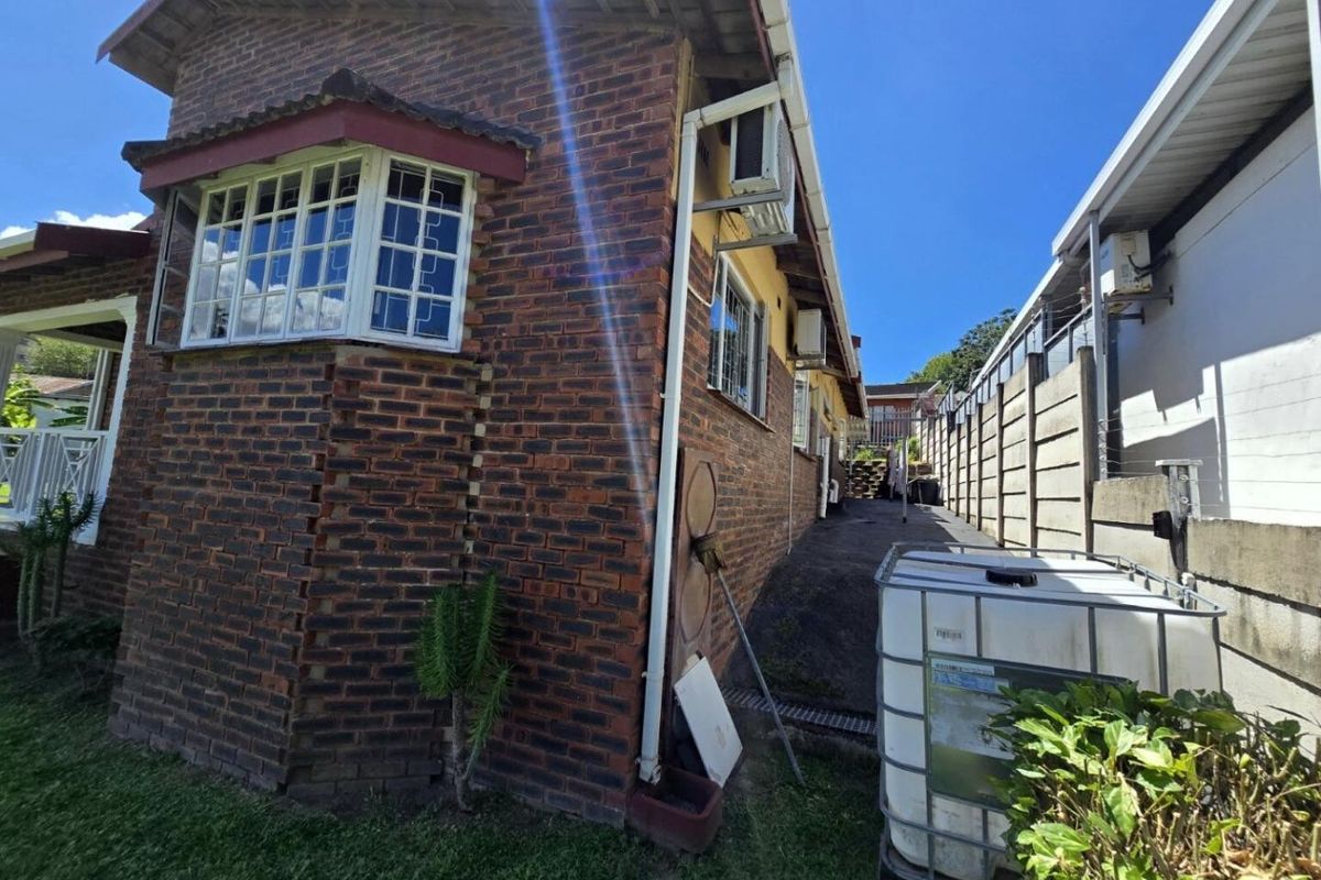 Side exterior view of a face brick house showing a bay window, guttering, and visible masonry cracking on the corner wall.
