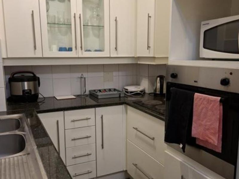 A functional kitchen featuring white cabinetry, granite countertops, a built-in oven, and a stainless steel double sink with a tiled backsplash.