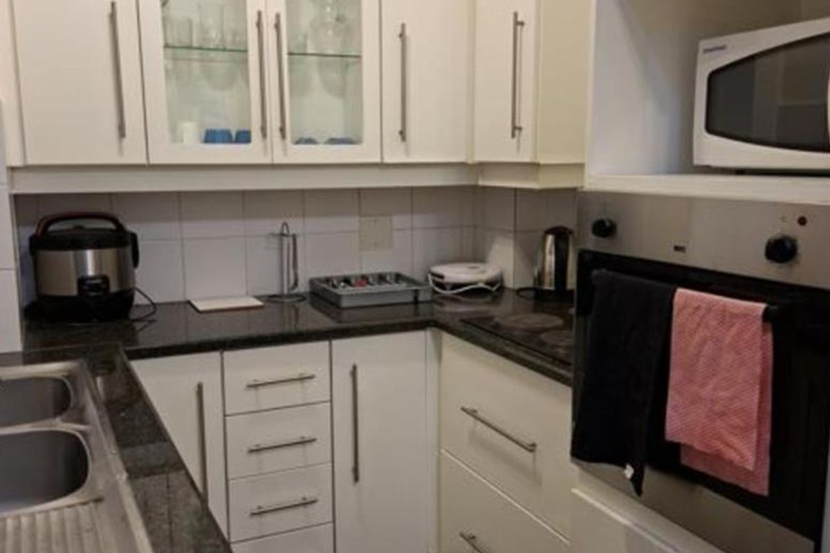 A functional kitchen featuring white cabinetry, granite countertops, a built-in oven, and a stainless steel double sink with a tiled backsplash.