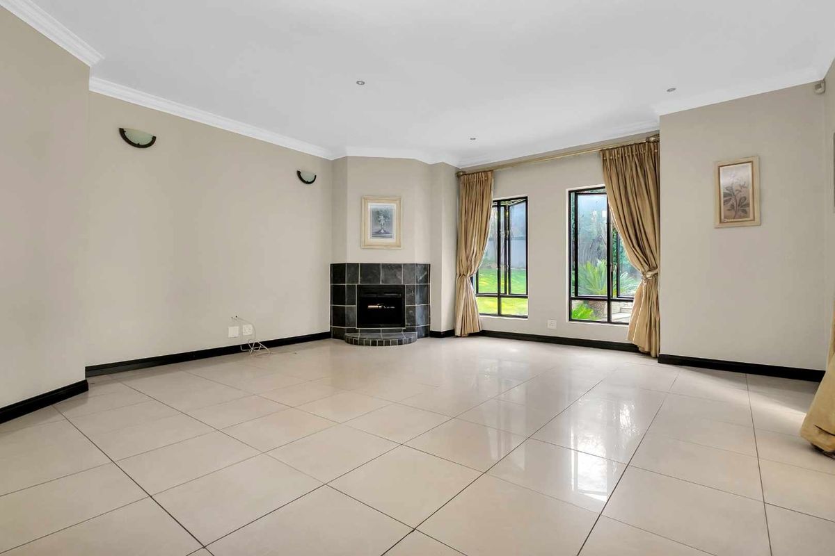 Spacious living room featuring large format floor tiles, a corner fireplace with tiled surround, and ample natural light through tall windows.
