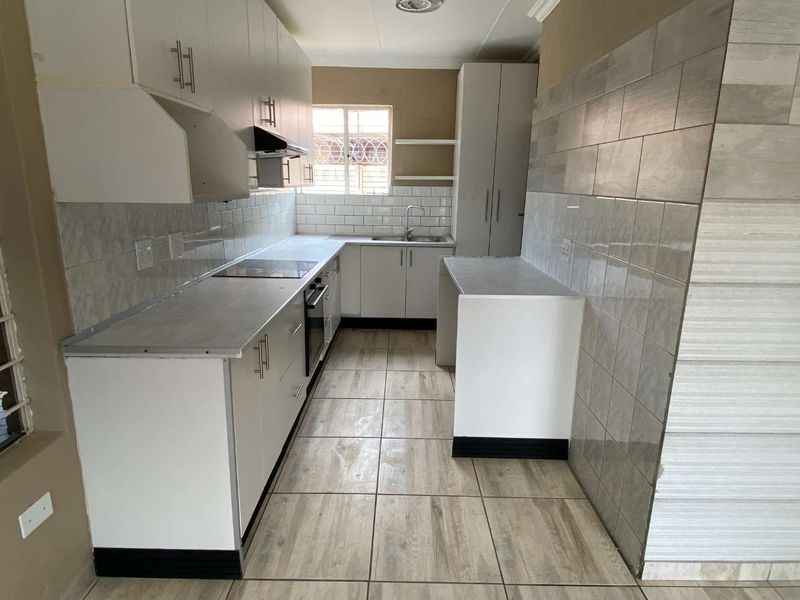 A functional kitchen featuring white cabinetry, laminate countertops, built-in oven and hob, tiled backsplash, and neutral floor tiles.