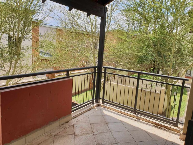A private balcony featuring tiled flooring, a metal safety balustrade, and a timber pergola, overlooking a landscaped garden area.