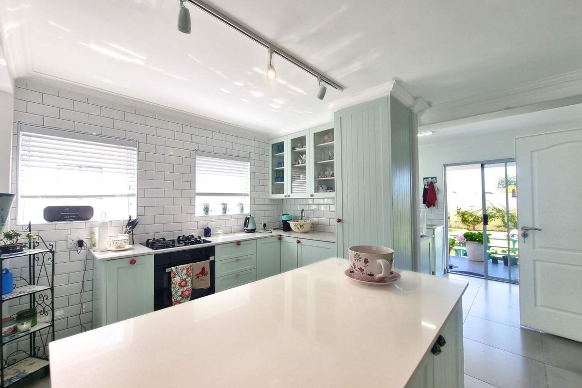 Bright kitchen featuring light green cabinetry, white subway tile backsplash, stone countertops, a central island, and track lighting, with direct access to the patio.