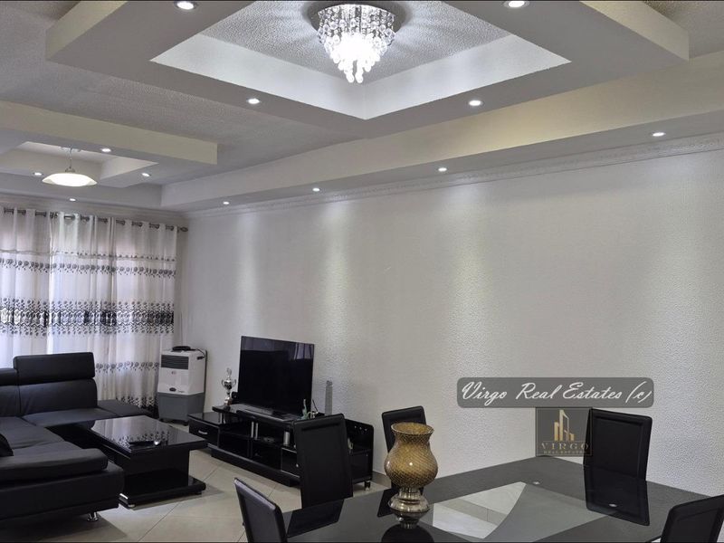 Spacious open-plan living and dining area featuring a sophisticated recessed ceiling with cove lighting, a crystal chandelier, and elegant crown molding.