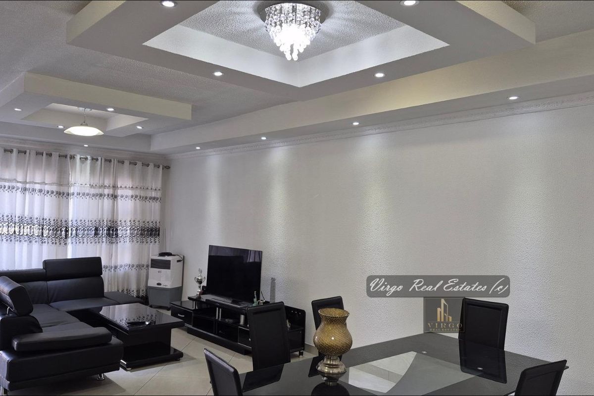 Spacious open-plan living and dining area featuring a sophisticated recessed ceiling with cove lighting, a crystal chandelier, and elegant crown molding.