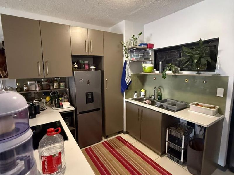 A functional kitchen featuring brown cabinetry, laminate countertops, a glass splashback, and a stainless steel sink, providing a practical workspace for daily cooking.