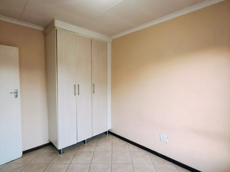 A clean, empty bedroom featuring neutral tiled flooring, a built-in wardrobe, and a simple ceiling light fixture.