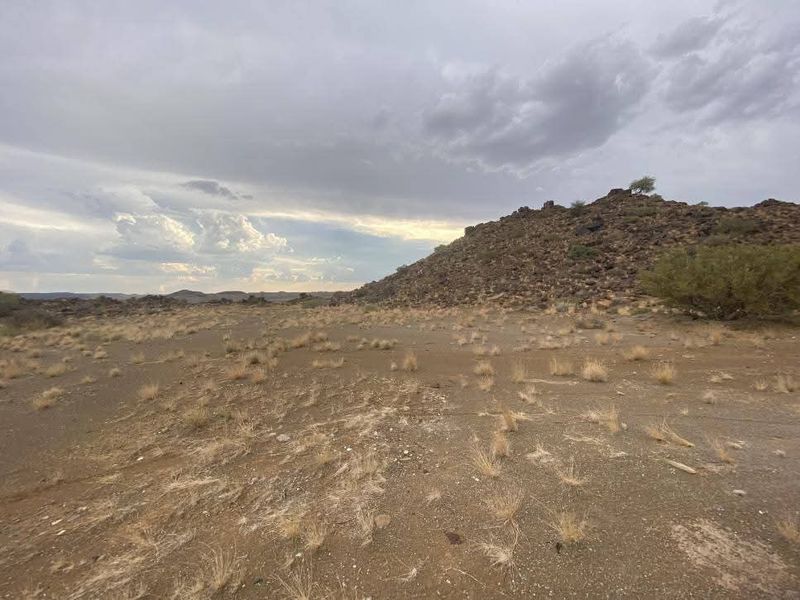 A wide-angle view of the vacant residential land featuring natural rocky terrain and open landscape under a cloudy sky.
