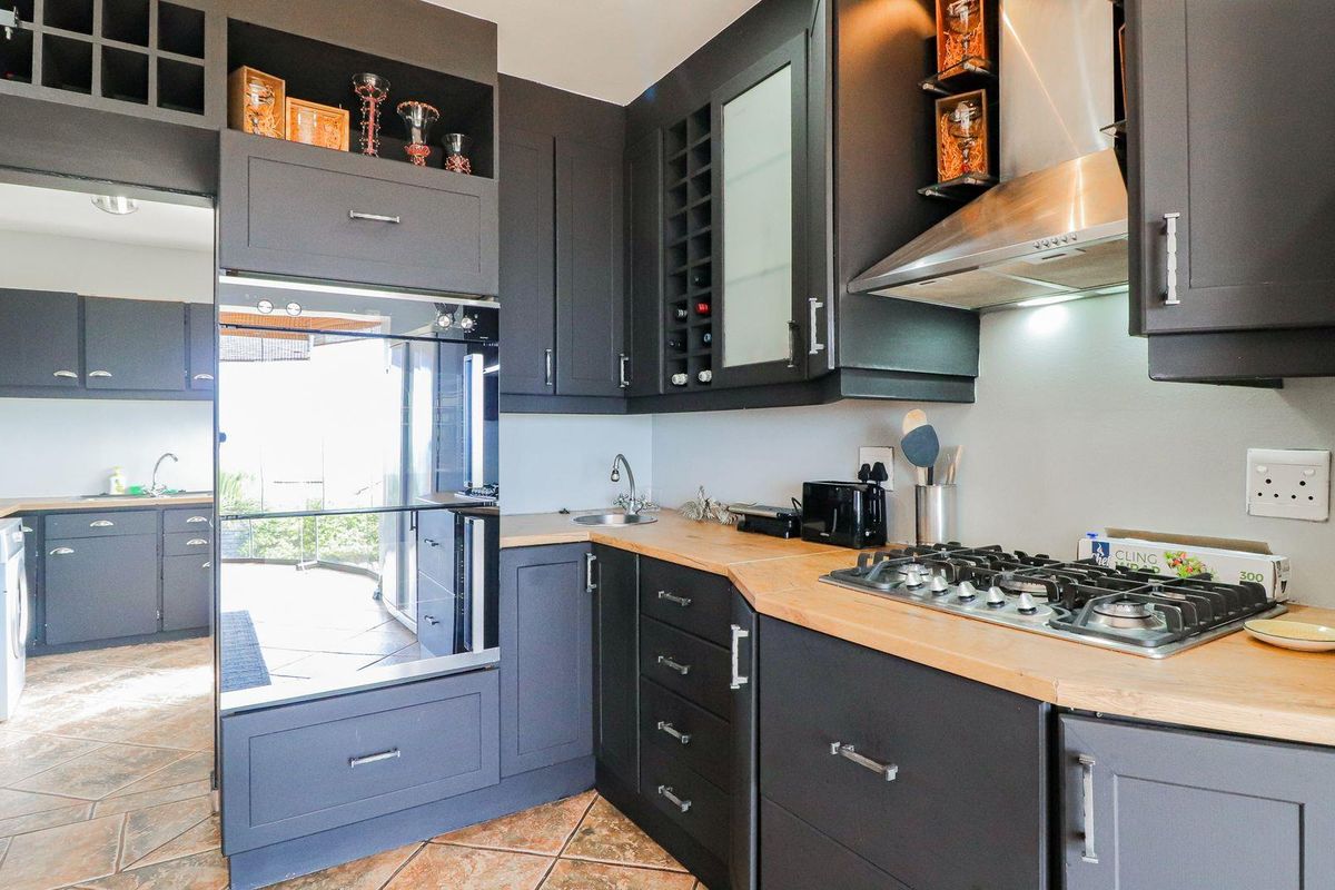 Modern kitchen featuring dark cabinetry, wooden countertops, a built-in oven, gas hob, and stainless steel extractor fan, with an adjacent scullery area.