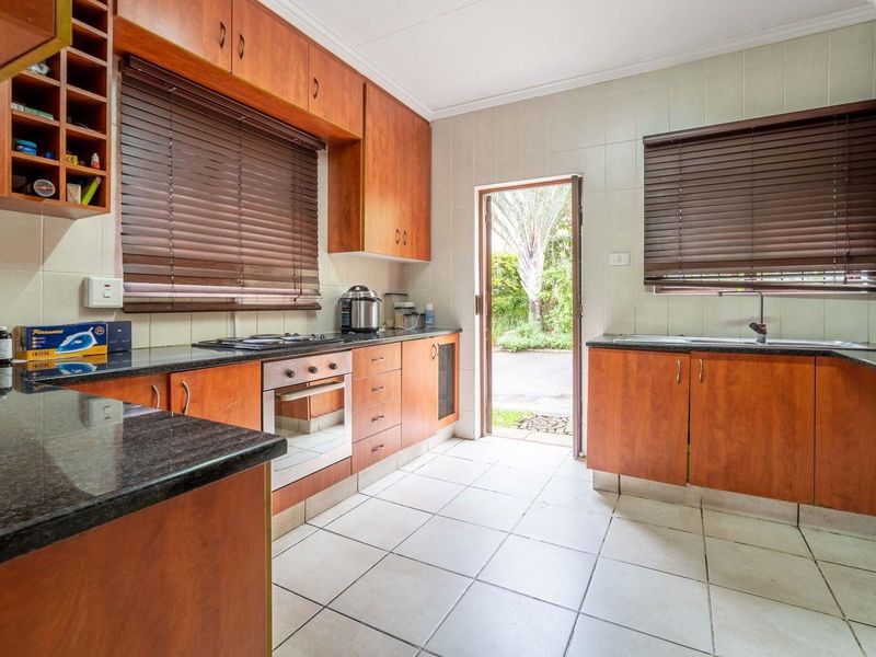 A functional kitchen featuring warm-toned wooden cabinetry, granite countertops, built-in oven and hob, and direct access to the exterior garden area.