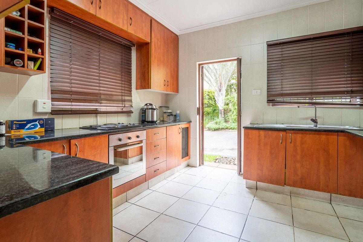 A functional kitchen featuring warm-toned wooden cabinetry, granite countertops, built-in oven and hob, and direct access to the exterior garden area.
