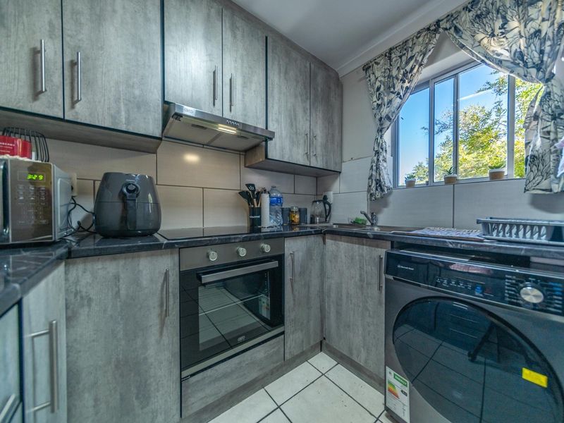 Compact kitchen featuring grey wood-look cabinetry, dark laminate countertops, built-in oven and hob, and tiled finishes.
