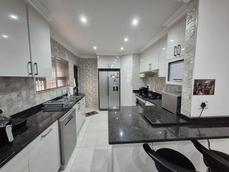 Modern kitchen featuring high-gloss cabinetry, granite countertops, integrated appliances, and a breakfast bar, finished with contemporary tiled splashbacks and recessed lighting.