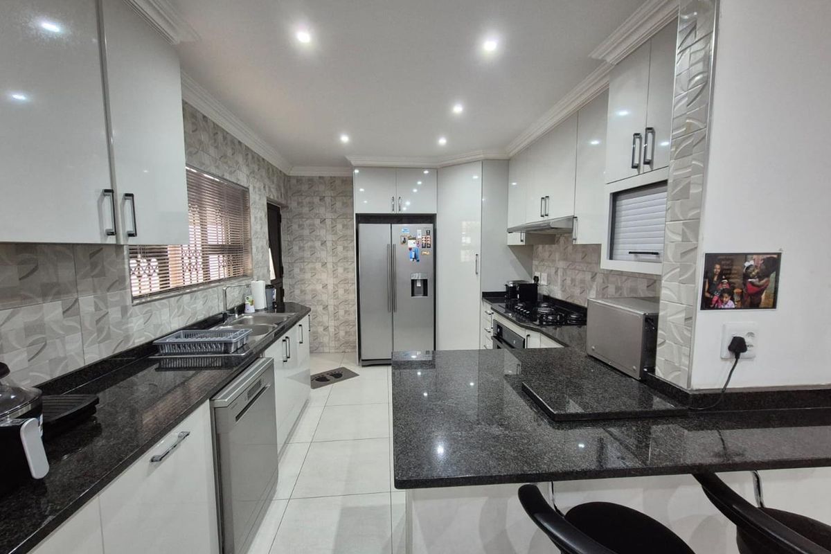 Modern kitchen featuring high-gloss cabinetry, granite countertops, integrated appliances, and a breakfast bar, finished with contemporary tiled splashbacks and recessed lighting.