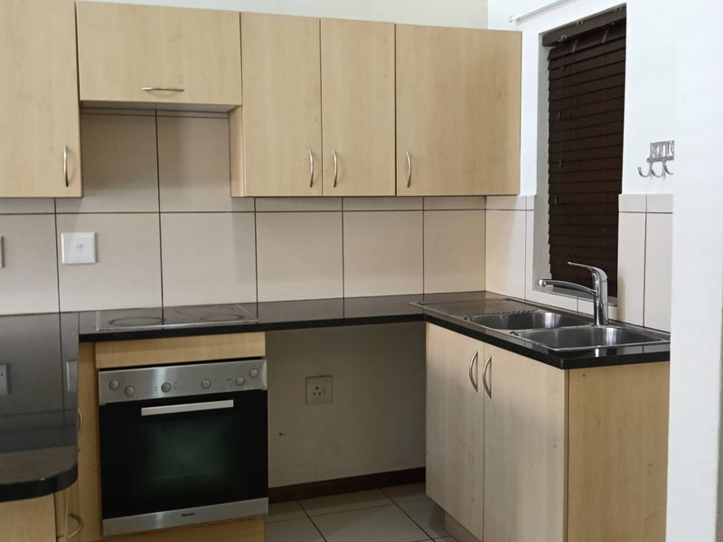 A functional kitchen featuring light wood cabinetry, granite countertops, a built-in oven, electric hob, and a stainless steel sink with tiled backsplash.