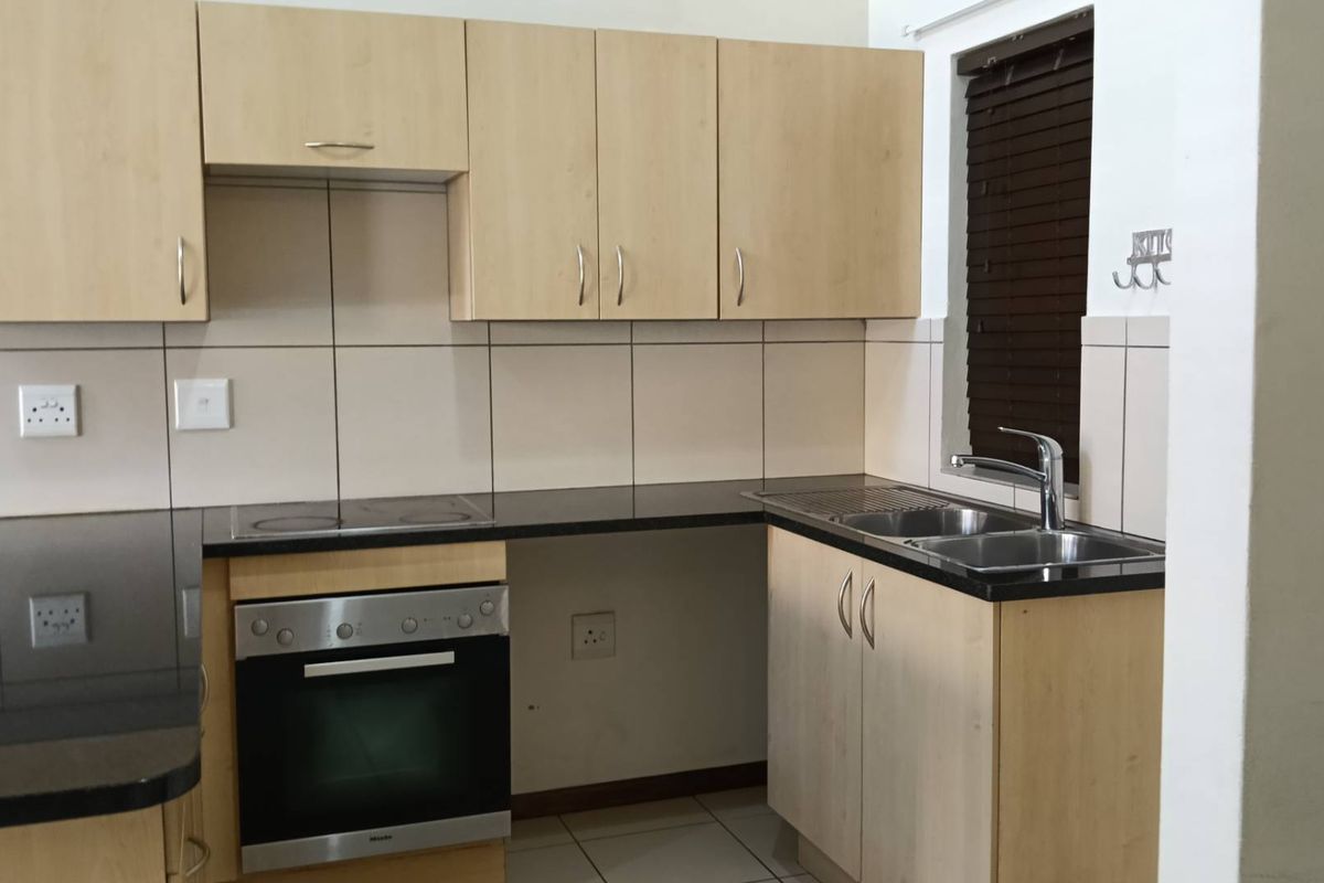 A functional kitchen featuring light wood cabinetry, granite countertops, a built-in oven, electric hob, and a stainless steel sink with tiled backsplash.