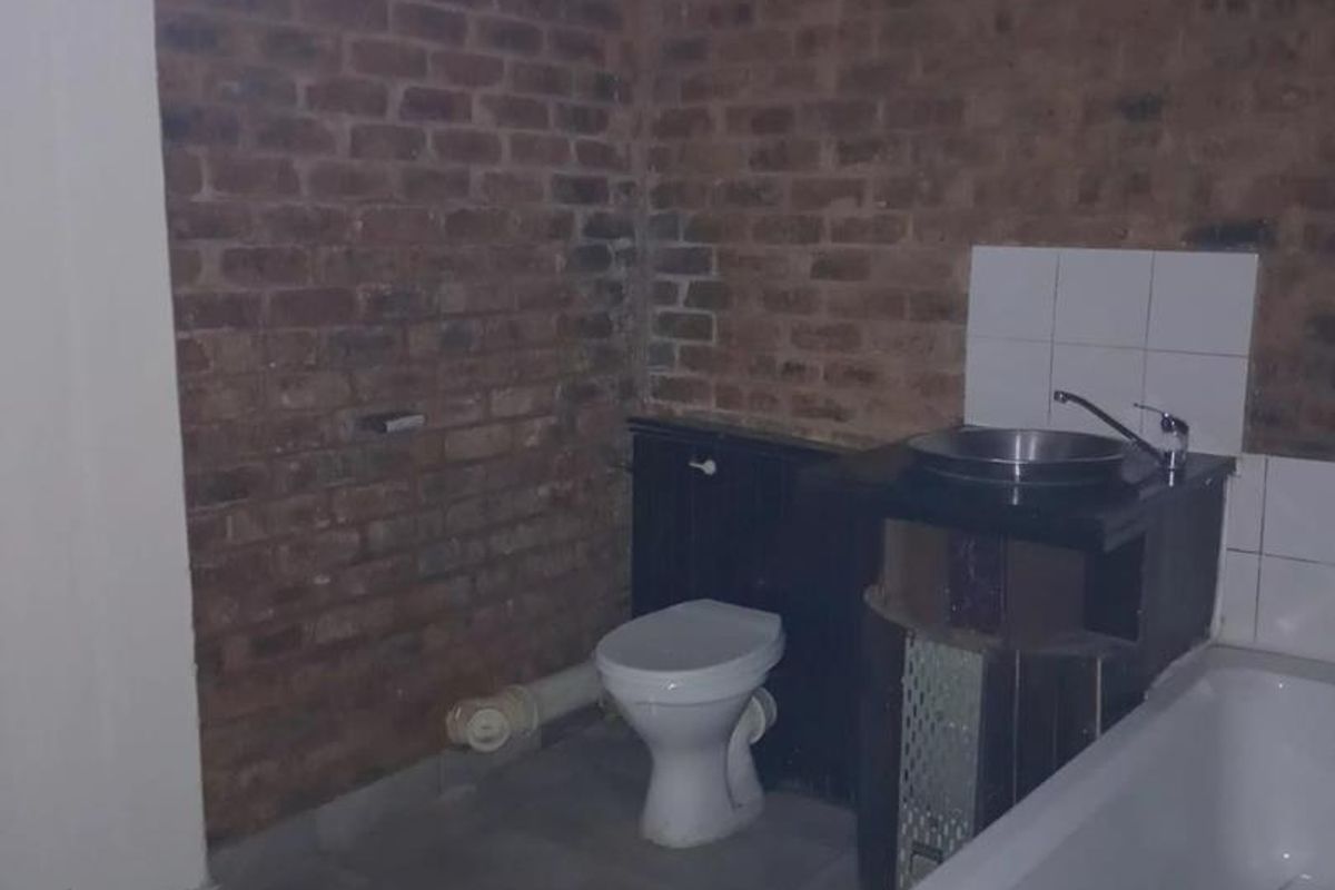 A bathroom featuring exposed brick walls, a bathtub, a vanity basin, and a toilet, currently in need of renovation and finishing.