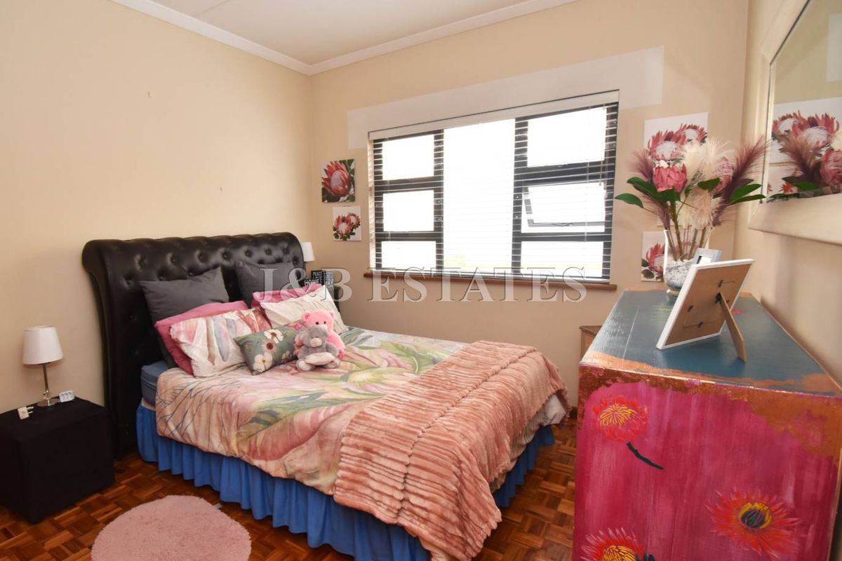 A bedroom featuring parquet flooring, a large window with fitted blinds, and neutral wall finishes.