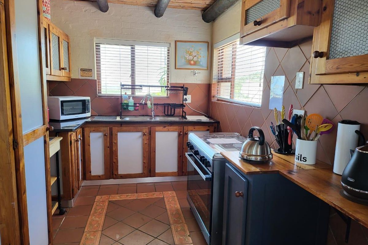 A rustic kitchen featuring wooden cabinetry, tiled countertops, a freestanding stove, and a unique exposed timber beam ceiling.
