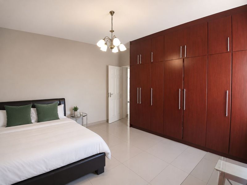 A well-maintained bedroom featuring large, floor-to-ceiling built-in wooden wardrobes, tiled flooring, and a classic chandelier light fixture.