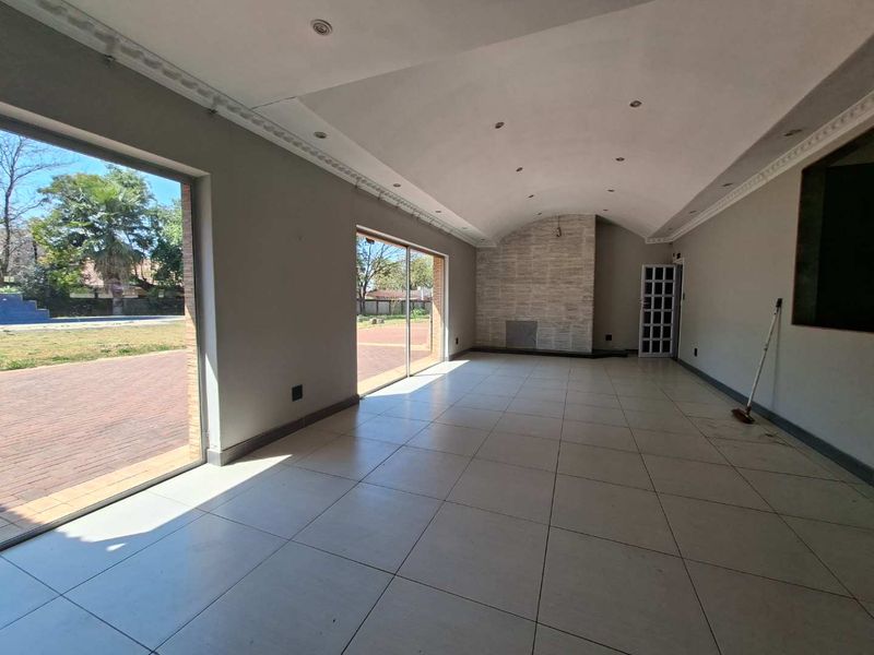 Spacious living area featuring a vaulted ceiling, tiled flooring, and a stone-clad fireplace, with large sliding doors providing direct access to the garden.