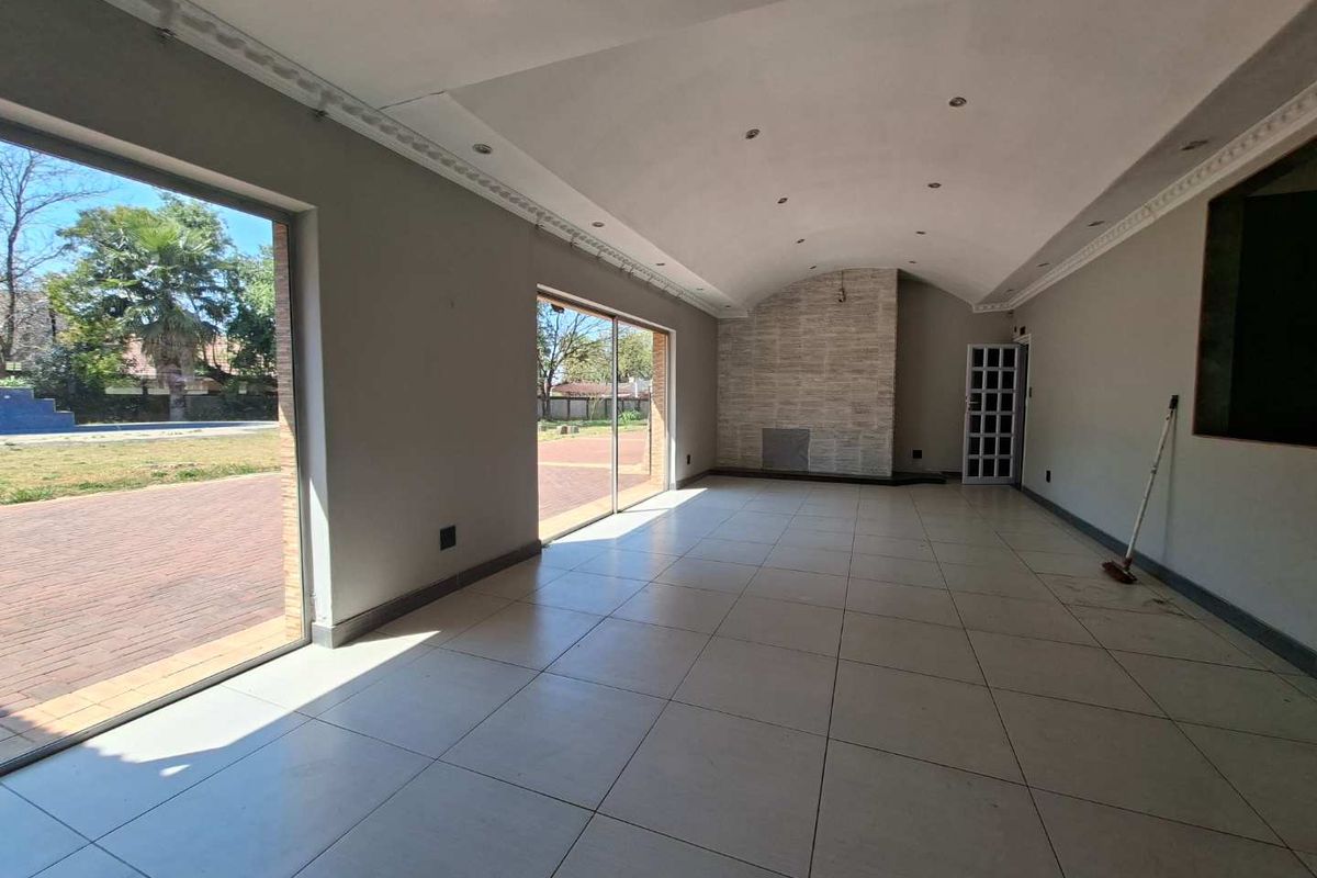 Spacious living area featuring a vaulted ceiling, tiled flooring, and a stone-clad fireplace, with large sliding doors providing direct access to the garden.