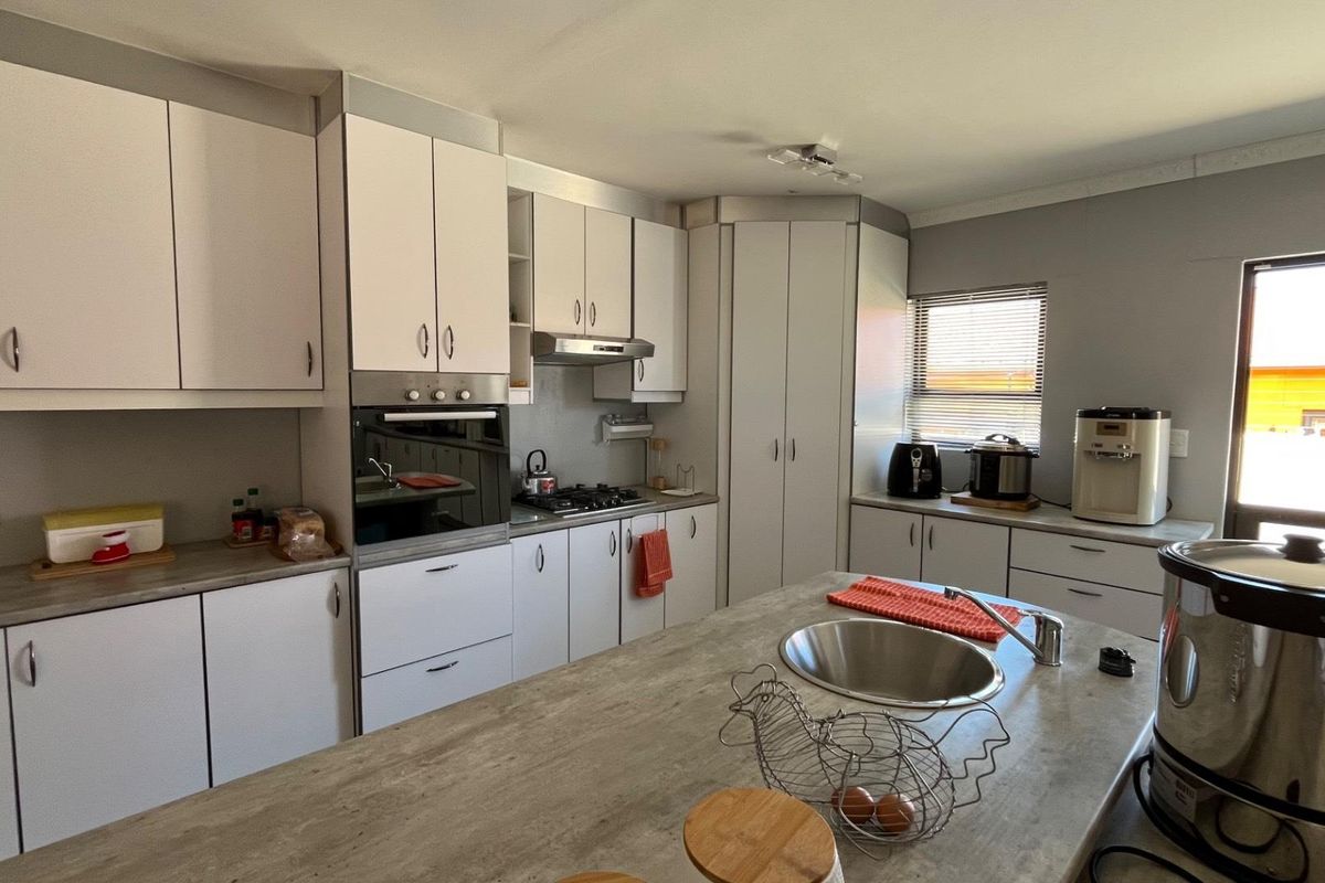 A functional kitchen featuring white cabinetry, a central island with a stainless steel sink, built-in oven, and gas hob with an extractor fan.
