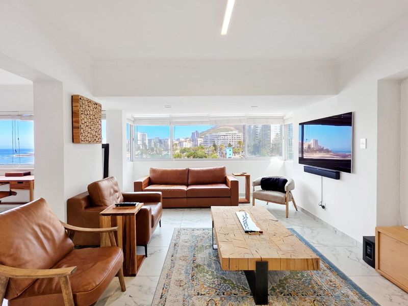 Bright and spacious living room featuring large windows with expansive city and coastal views, marble-look flooring, and modern recessed lighting.