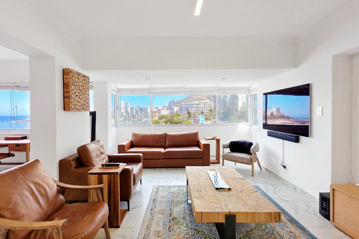 Bright and spacious living room featuring large windows with expansive city and coastal views, marble-look flooring, and modern recessed lighting.