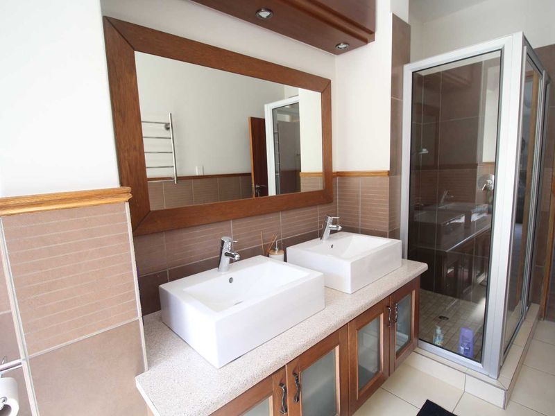 Modern bathroom featuring a double vanity with vessel sinks, a glass-enclosed shower, and neutral tiled finishes throughout.