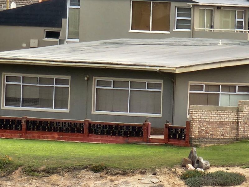Rear view of a single-story residence featuring a flat roof, large windows, and a combination of brick and decorative breeze block boundary walls.