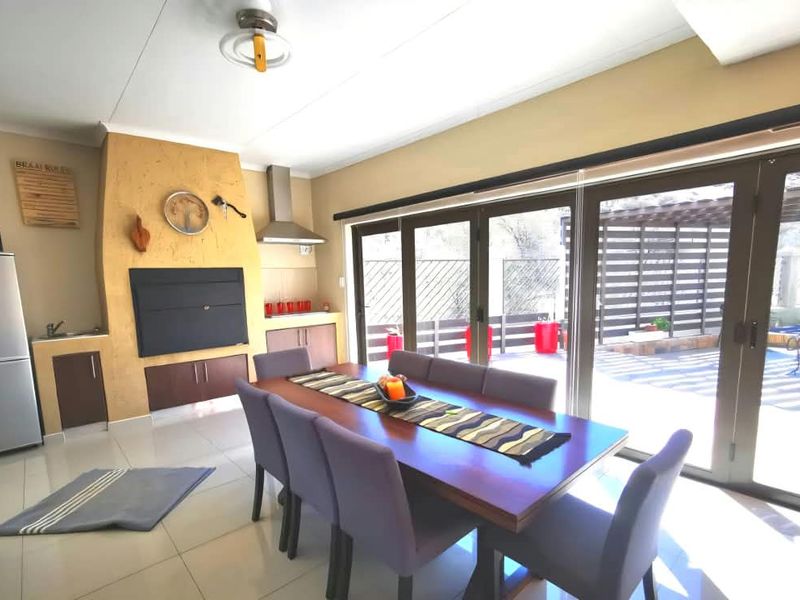 Open-plan dining area featuring a built-in braai, tiled flooring, and large sliding glass doors providing seamless access to the outdoor patio and pool area.