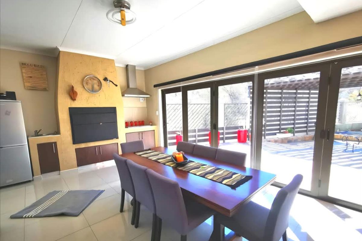 Open-plan dining area featuring a built-in braai, tiled flooring, and large sliding glass doors providing seamless access to the outdoor patio and pool area.