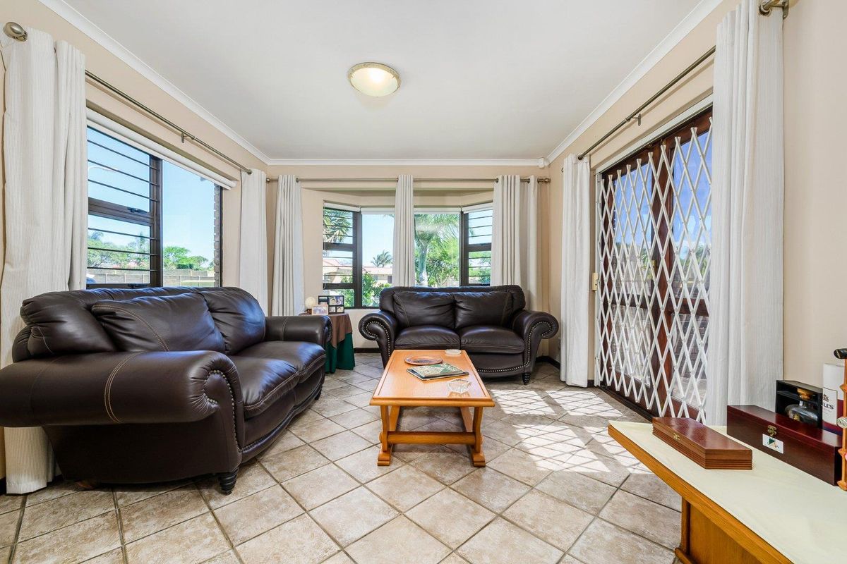A bright living room featuring tiled flooring, large windows, and a sliding glass door with a security gate, providing access to the outdoor area.