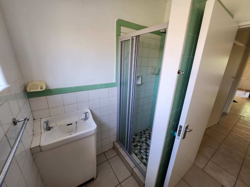 A functional bathroom featuring a shower enclosure, pedestal basin, and tiled finishes, offering a blank canvas for modern renovation and aesthetic updates.