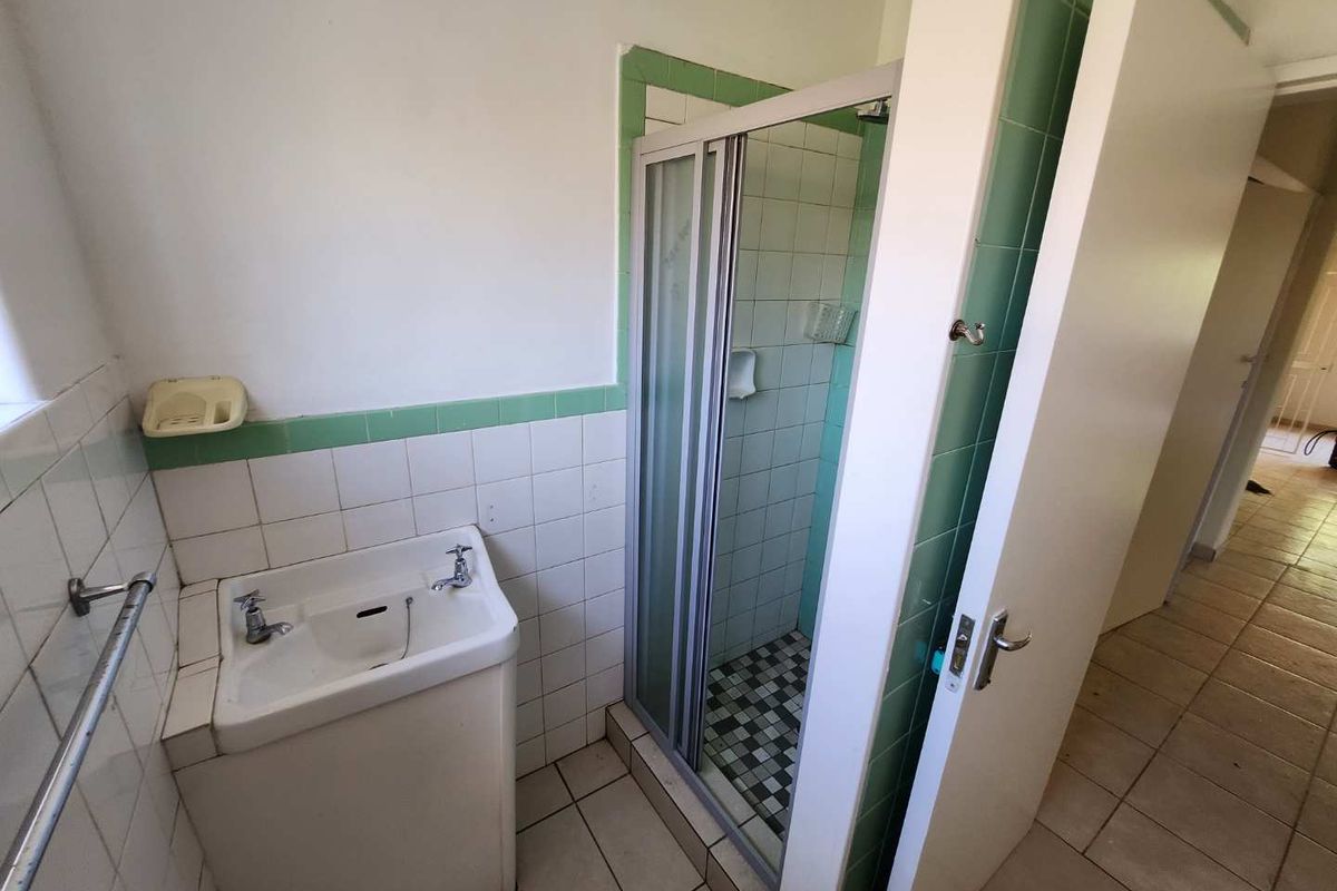 A functional bathroom featuring a shower enclosure, pedestal basin, and tiled finishes, offering a blank canvas for modern renovation and aesthetic updates.