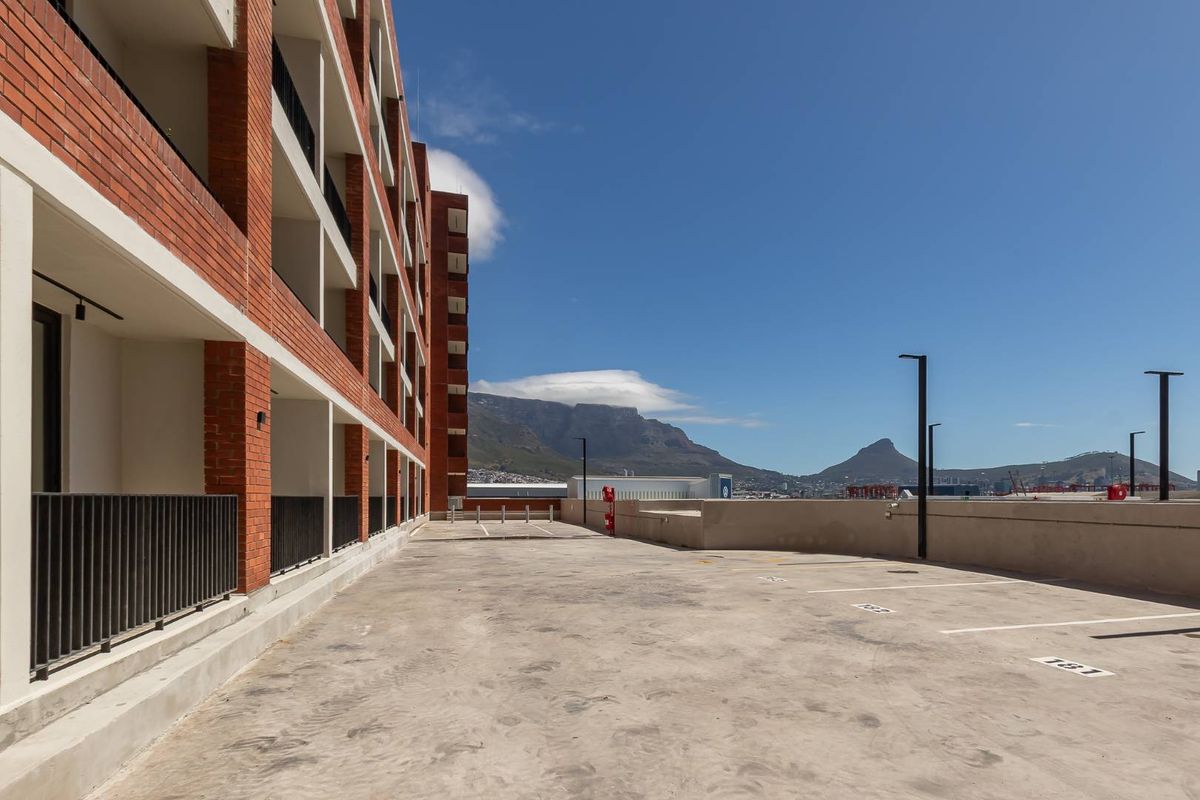 An exterior view of the apartment building featuring a paved parking area with marked bays, brick facade, and mountain views.