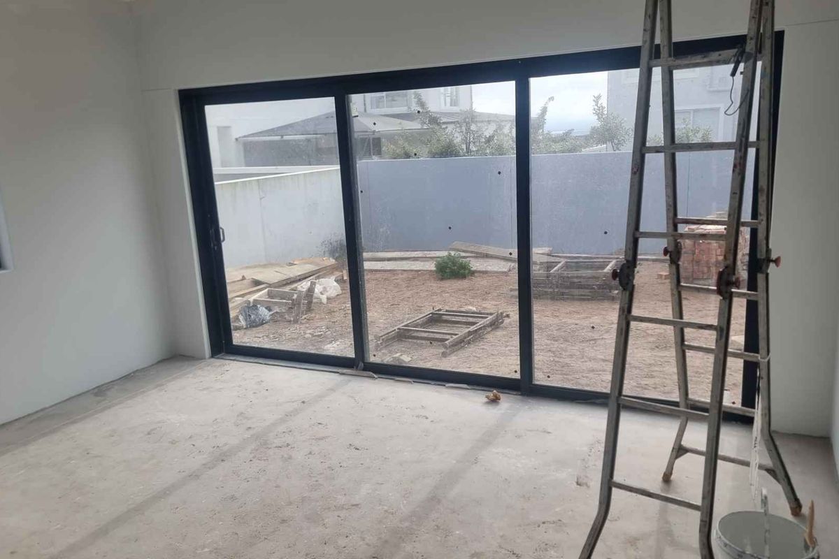 An unfinished interior living space featuring large black-framed sliding glass doors that open onto a rear yard area currently under development.