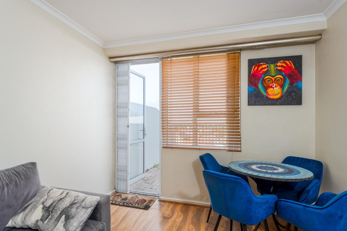 A living area featuring wood-look flooring, a window with fitted blinds, and a security gate providing access to an outdoor space.