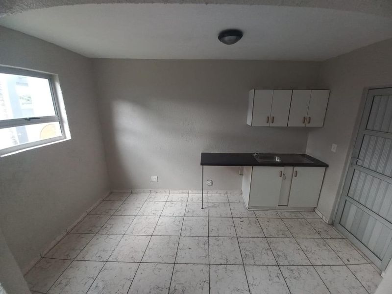 A compact, empty kitchen area featuring basic white cabinetry, a stainless steel sink, and tiled flooring, offering a blank canvas for potential renovation.