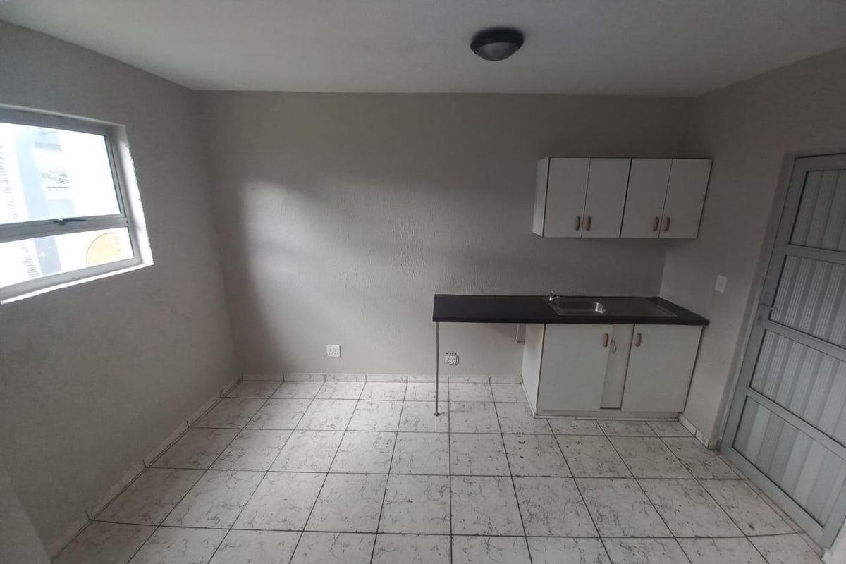 A compact, empty kitchen area featuring basic white cabinetry, a stainless steel sink, and tiled flooring, offering a blank canvas for potential renovation.