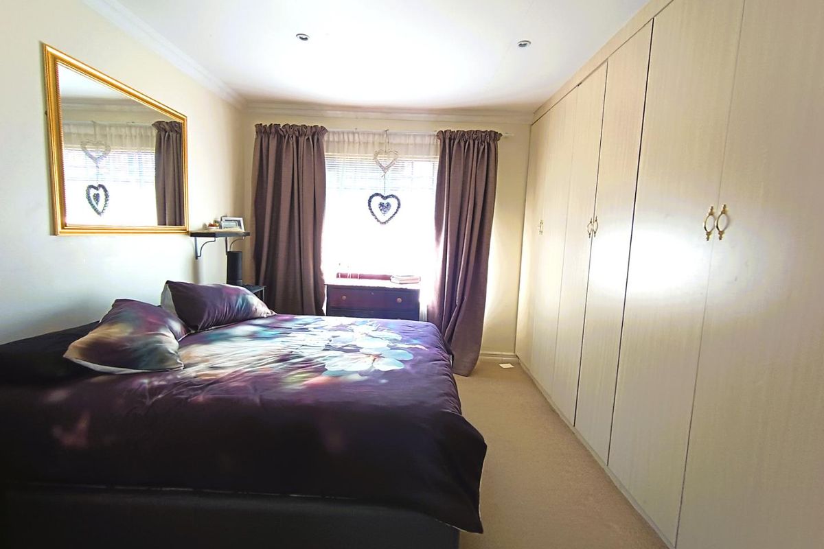 A well-lit bedroom featuring extensive floor-to-ceiling built-in wardrobes, neutral carpeting, and recessed ceiling lighting.