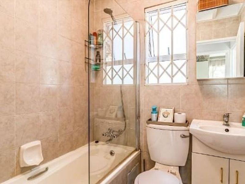 A functional bathroom featuring a bathtub with a glass screen, a vanity basin with storage, and tiled wall finishes.
